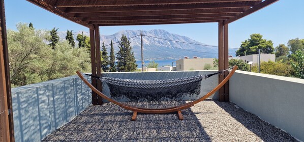 A hammock under a wooden pergola with a view of mountains and a body of water. - NIMA Suites (Palairos)