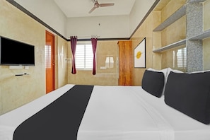Quarto de hotel com cama, televisão de tela plana, ventilador de teto e janela com cortinas.