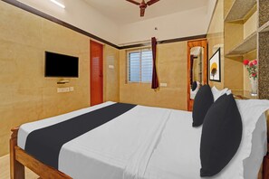 Una habitación de hotel con una cama, televisión montada en la pared, una ventana con cortinas y un ventilador de techo.