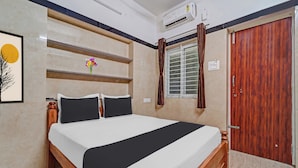 A bedroom with a bed, a wooden wardrobe, an air conditioning unit, a window with curtains, and a wall-mounted shelf with flowers. - Hotel O Jaganath Nagar Near Hopes (Coimbatore)