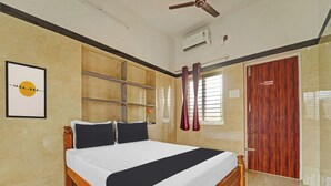 A hotel room with a bed, a ceiling fan, an air conditioning unit, a window with curtains, and a wooden door. - Hotel O Jaganath Nagar Near Hopes (Coimbatore)