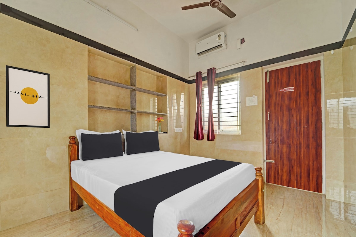 Quarto de hotel com cama, ventoinha no teto, aparelho de ar condicionado, janela com cortinas e porta de madeira.