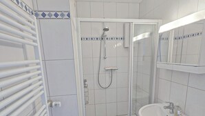 Un baño moderno con cabina de ducha de vidrio, un lavabo blanco y un taburete pequeño.