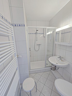 A modern bathroom with a glass-enclosed shower, a white sink, and a small stool. - Vrbo Property (Großenbrode)