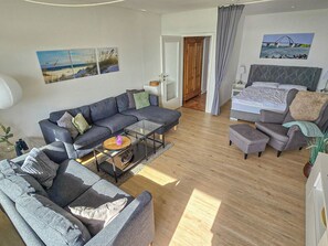 A modern living room with a sofa, a coffee table, and a bed with a headboard. - Vrbo Property (Großenbrode)