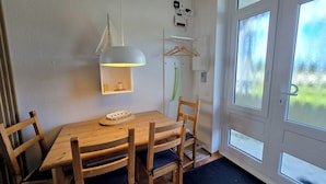 Un comedor con una mesa y sillas de madera, una lámpara colgante y vistas a través de un ventanal.