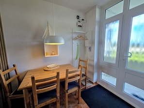 A dining area with a wooden table and chairs, a hanging light fixture, and a view through a glass door. - Vrbo Property (Großenbrode)