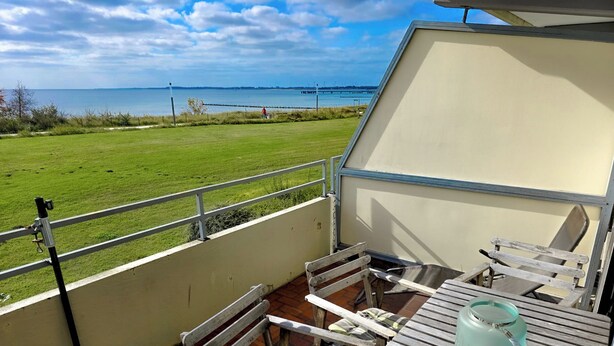 Un balcón con mesa y sillas, con vistas a una zona verde y una masa de agua.