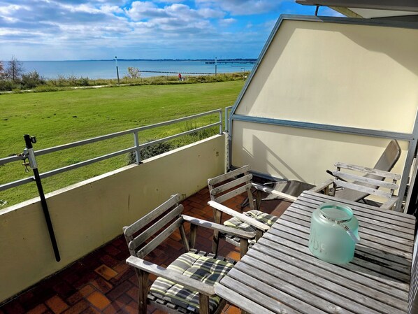 A balcony with a table and chairs, overlooking a grassy area and a body of water. - Vrbo Property (Großenbrode)