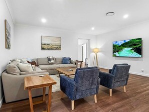 A modern living room with a sofa, coffee table, and armchairs, a flat-screen TV, and a floor lamp.