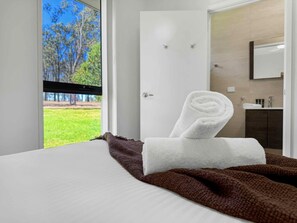 Quarto de hotel com cama, janela com vista para árvores e banheiro com espelho e pia.