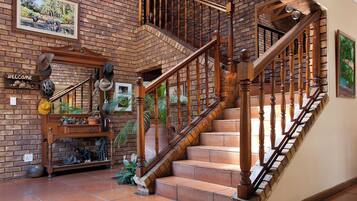 Una escalera de madera con un fondo de pared de ladrillo, un letrero de bienvenida y varios objetos decorativos, incluyendo sombreros y un cuadro enmarcado.