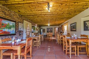 A restaurant with a bamboo ceiling, wooden tables, and chairs, and paintings on the walls.