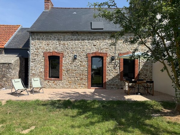 Un bâtiment en pierre doté de deux portes et d’un petit patio aménagé avec du mobilier d’extérieur.