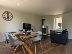 Un espace de vie moderne comprenant une table à manger en verre, des sièges confortables, une cheminée et une grande horloge murale.