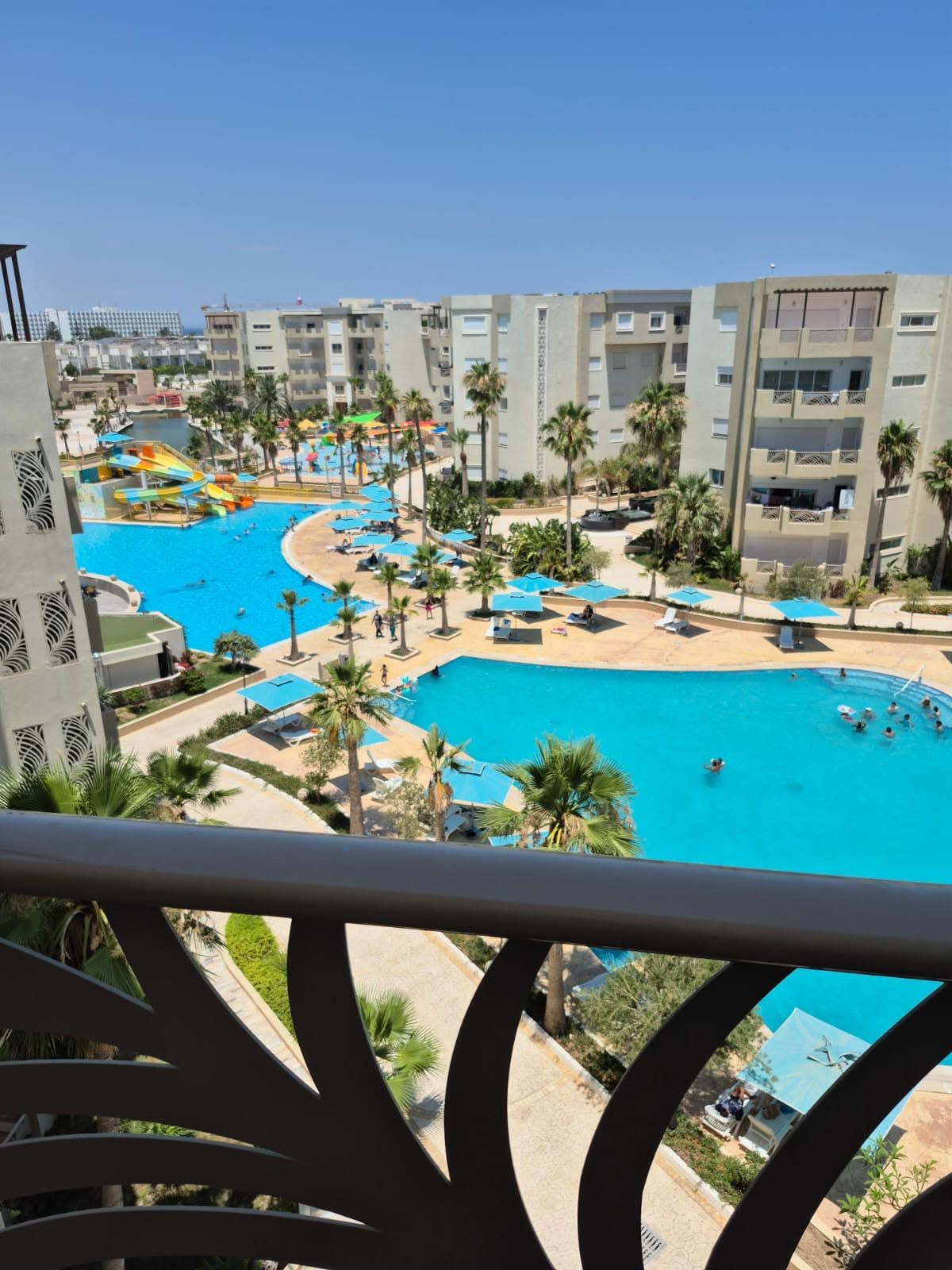 A resort with multiple swimming pools, palm trees, and a view of high-rise buildings.