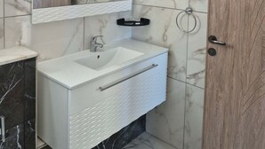 A bathroom with a white vanity, a mirror, and a wooden door. - Vrbo Property (Monastir)