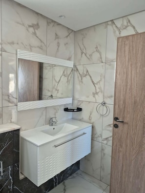 Un bany amb un lavabo blanc, un mirall i una porta de fusta.