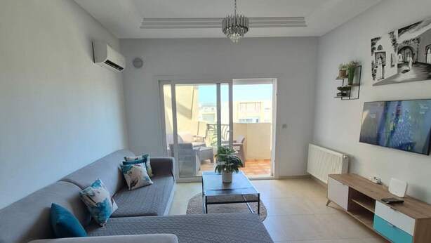 A modern living room with a grey sofa, a coffee table, and a TV on a wooden stand. - Vrbo Property (Monastir)
