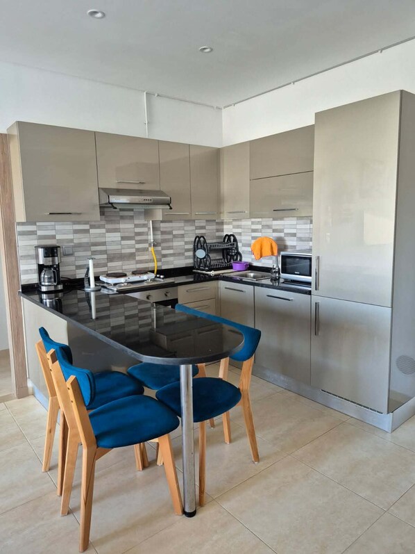 A modern kitchen with a central island, stainless steel appliances, and a dining area with blue chairs.