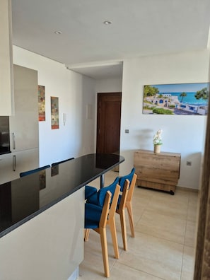 Cuina moderna amb taulell negre, cadires de fusta i armari de fusta.