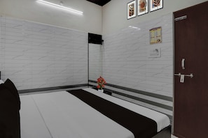 Una camera d'albergo con un letto, uno specchio, una lampada a parete, una porta e un addobbo murale.