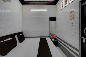 Una habitación de hotel con cama, una mesita, un espejo, una lámpara de pared y una puerta.