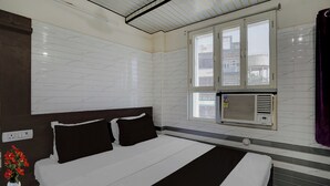 Ein Hotelzimmer mit Bett, Fenster und Klimaanlage, sowie eine Wandsteckdose.