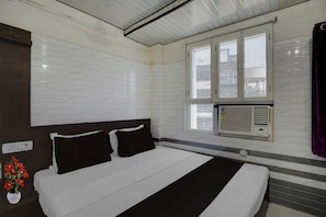 Una camera d'albergo con un letto, una finestra e un condizionatore d'aria, oltre a una presa elettrica a parete.