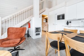 Ein modernes Interieur mit einer Treppe, einem Essbereich mit Tisch und Stühlen sowie einer Küche mit weißen Schränken und Geräten.