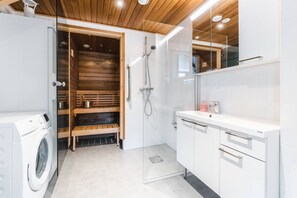 Ein modernes Badezimmer mit einer Holzsauna, einer Waschmaschine und einem weißen Waschtisch mit Spiegel.