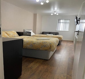 A hotel room with two beds, a desk, and a window with blinds. - Standard Triple Room - Shared (Manchester)