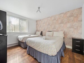 A bedroom with two beds, a radiator, a window with blinds, and a ceiling fan. - Standard Triple Room - Shared (Manchester)