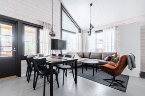 Een moderne woonkamer met een bank, een eettafel met stoelen, een televisie en een groot raam.