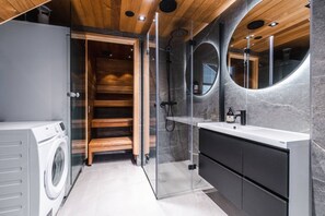 Een moderne badkamer met een houten sauna, een douche met glazen wanden en een wastafelmeubel met spiegel.