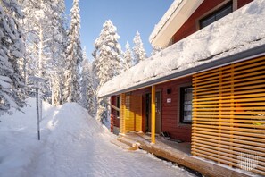 A red building with a wooden porch and a snow-covered roof, surrounded by snow-laden trees. - SointuiLevi Premium A58 by Holiday in Lapland (Levi)