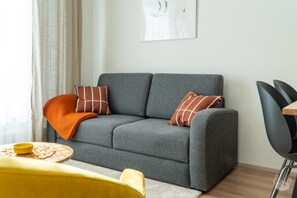 Ein graues Sofa mit zwei gemusterten Kissen, ein gelber Sessel und ein kleiner runder Tisch mit einer gelben Schüssel.