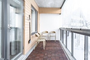A balcony with a brick floor, two chairs, and a window with a view of a snowy landscape. - Aurinkorinne 2 A by Holiday in Lapland (Levi)