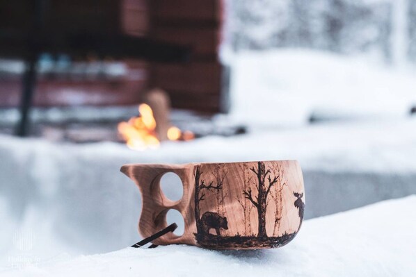 Ein hölzerner Becher mit einem Baum- und Tiermotiv, auf einer verschneiten Fläche platziert.