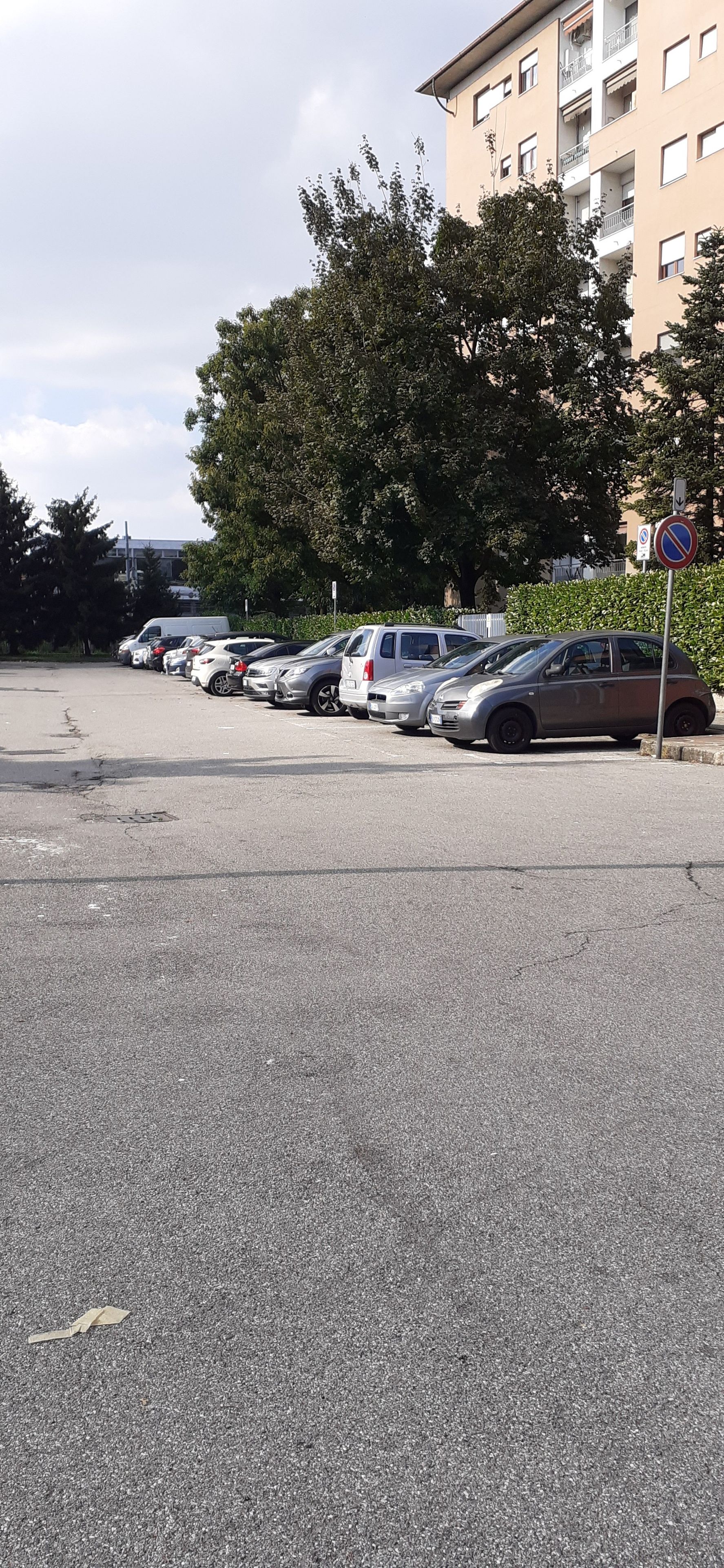 Un parking où de nombreuses voitures sont garées en rangées, un panneau indiquant qu’il est interdit de se garer, et un bâtiment avec des balcons en arrière-plan.
