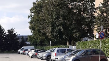 Un parking où de nombreuses voitures sont garées en rangées, un panneau indiquant qu’il est interdit de se garer, et un bâtiment avec des balcons en arrière-plan.