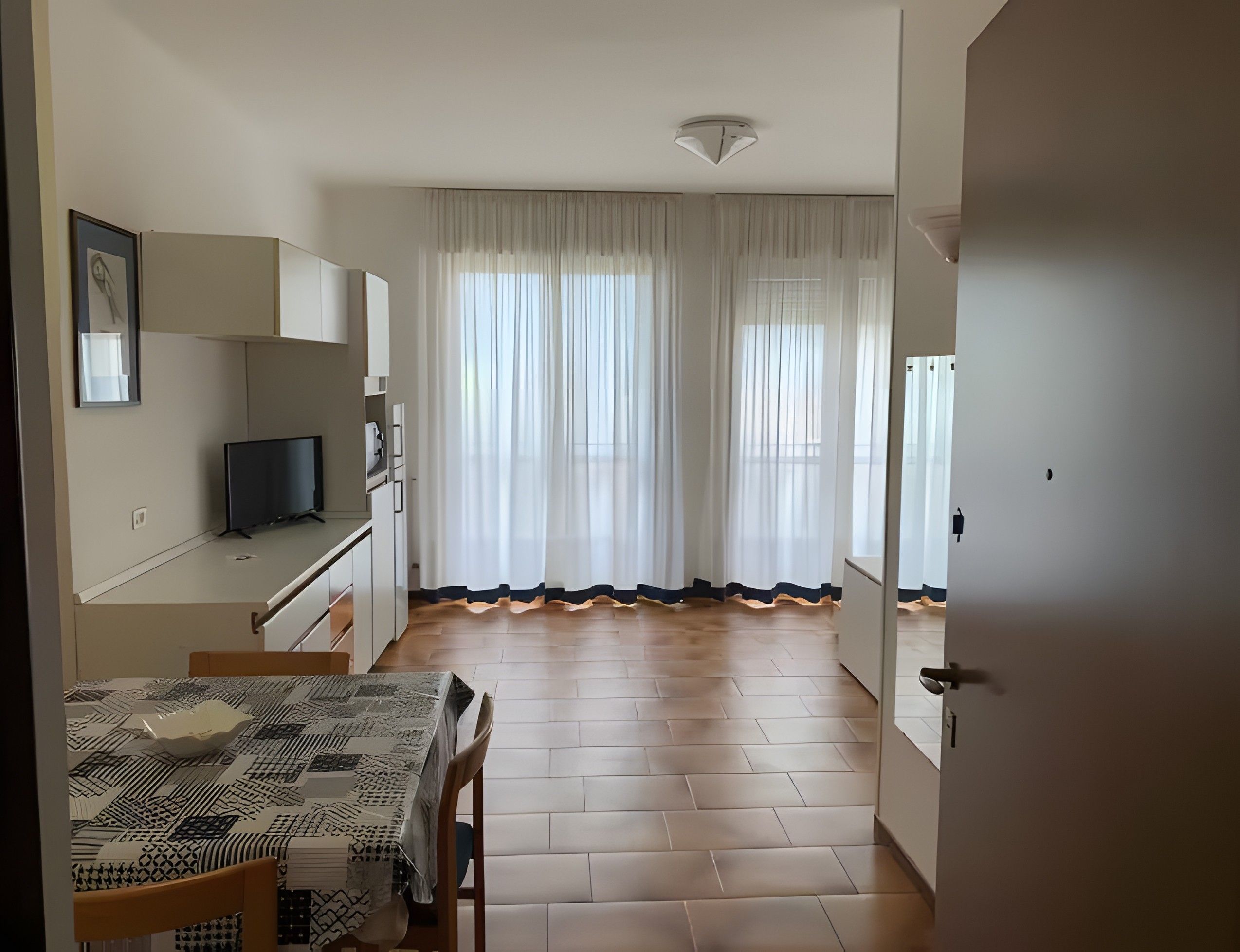 Een eethoek met een tafel en stoelen, een televisie, en een keuken met kasten en een koelkast.