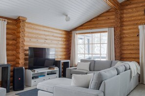 L'intérieur d'une cabane en rondins, avec un téléviseur, un canapé et des haut-parleurs.