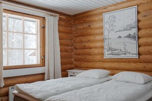 Ein Schlafzimmer einer Holzhütte mit einem Bett, einem Nachttisch, einem Fenster mit Vorhängen und einer Wanddekoration.