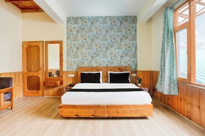 A wooden-framed bed with a patterned wall behind it, a wooden wardrobe, and a window with curtains. - Hotel O Model Town Road (Manali)