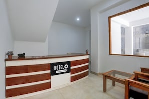 A hotel reception desk with a sign indicating it is company-serviced. There is a wooden bench and a small potted plant on the desk. - Hotel O Model Town Road (Manali)