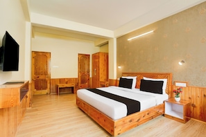 A hotel room with a wooden bed, a bedside table, a small bedside lamp, and a television mounted on the wall. - Hotel O Model Town Road (Manali)