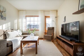 A living room with a sofa, armchair, coffee table, TV, and windows with curtains. - Alppilevi 1B1 by Holiday in Lapland (Levi)