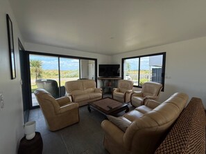 Ein modernes Wohnzimmer mit Ledersofas, einem Flachbildfernseher und großen Fenstern mit Blick ins Freie.