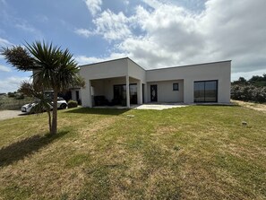 Ein modernes, zweistöckiges Haus mit Flachdach, großen Fenstern und einer überdachten Terrasse.